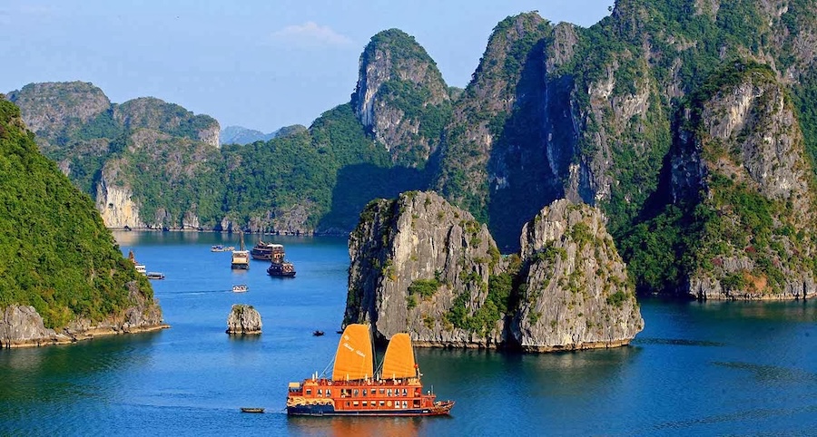 A traditional junk boat sailing on Ha Long Bay at sunset