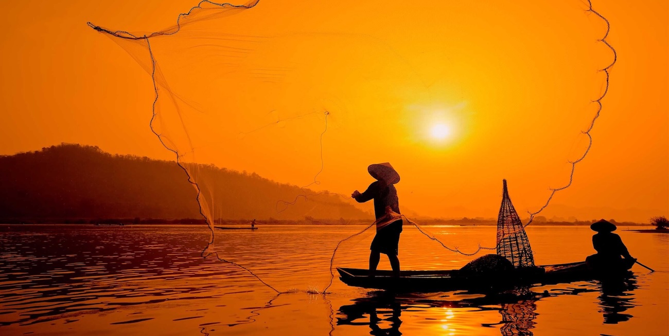 A woman in a traditional conical hat rowing a sampan boat through a lush Mekong Delta canal