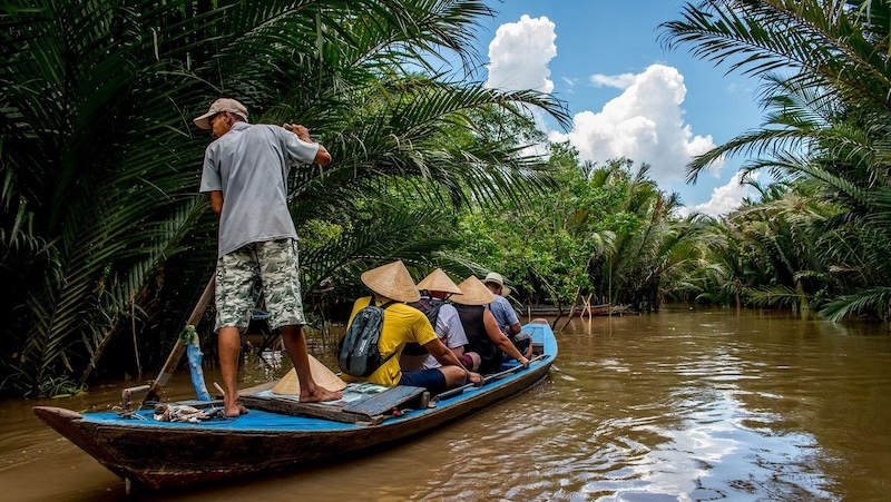 A peaceful sampan boat ride through a narrow, palm-fringed canal