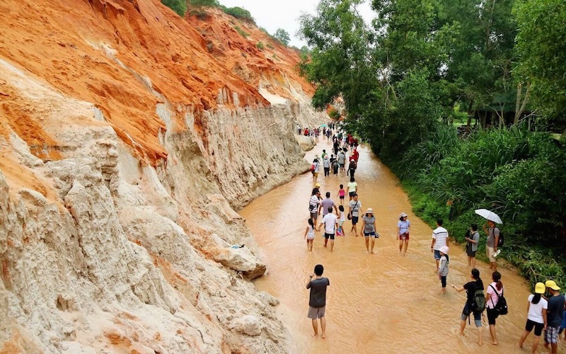 A person wading through the shallow red water of the Fairy Stream